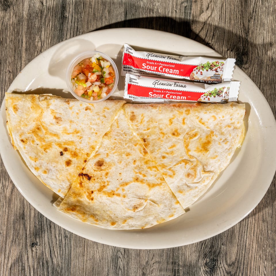 Grilled cheese quesadilla served with pico de gallo and two sour cream packets on a white plate.