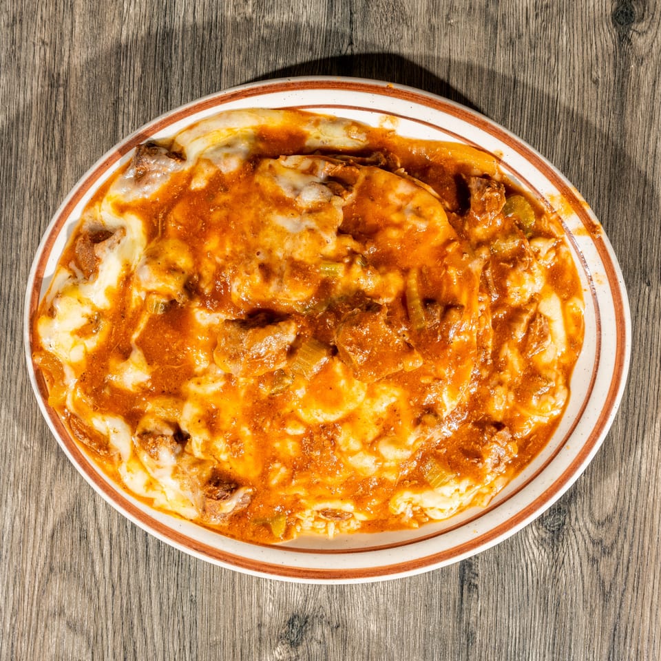 Cheesy baked casserole with mushrooms and vegetables in tomato sauce, served on an oval plate atop a wooden table.