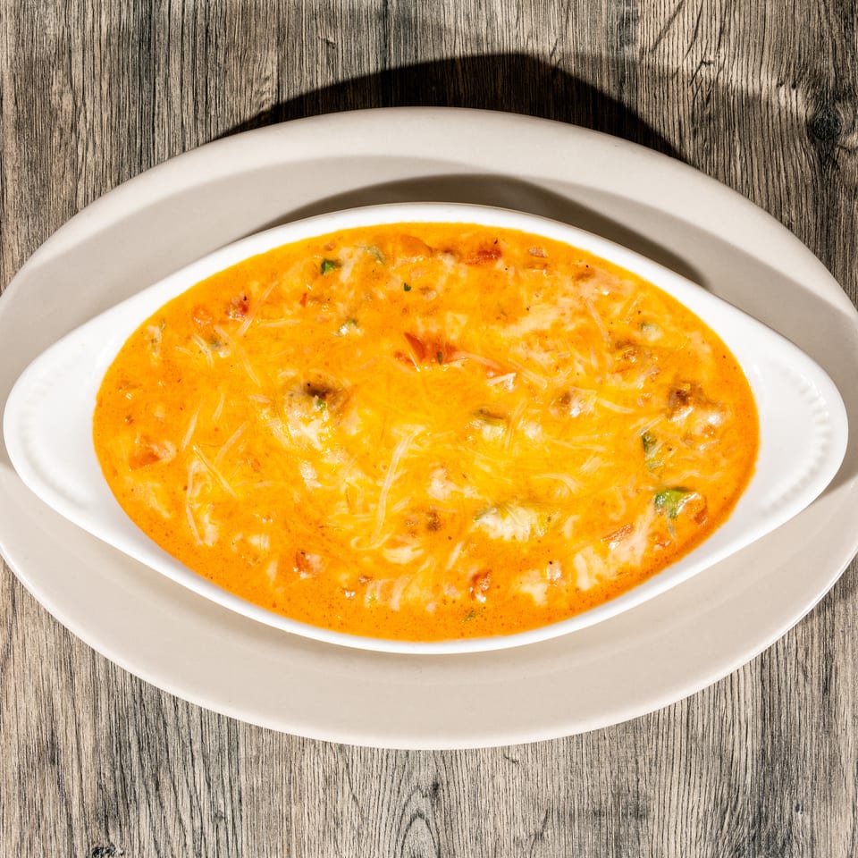 Creamy orange soup with shredded cheese and herbs served in an oval white dish on a wooden table.