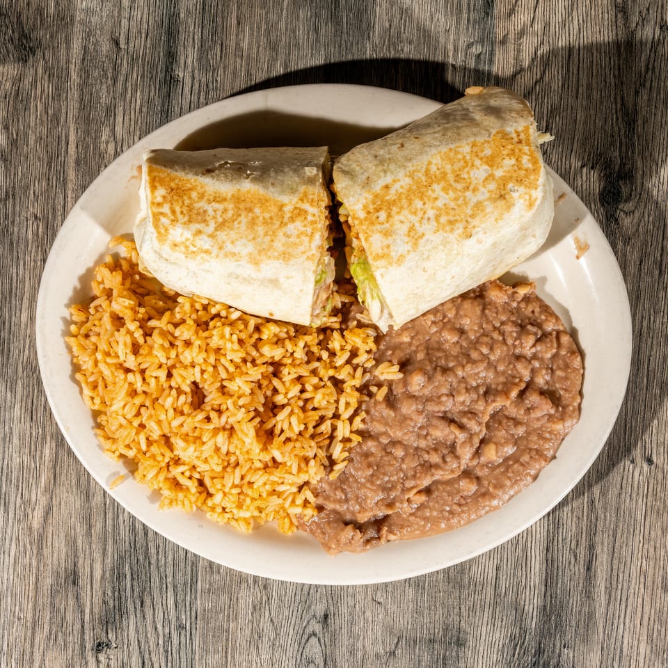 Plate of two toasted burritos served with Mexican rice and refried beans on a wooden table.