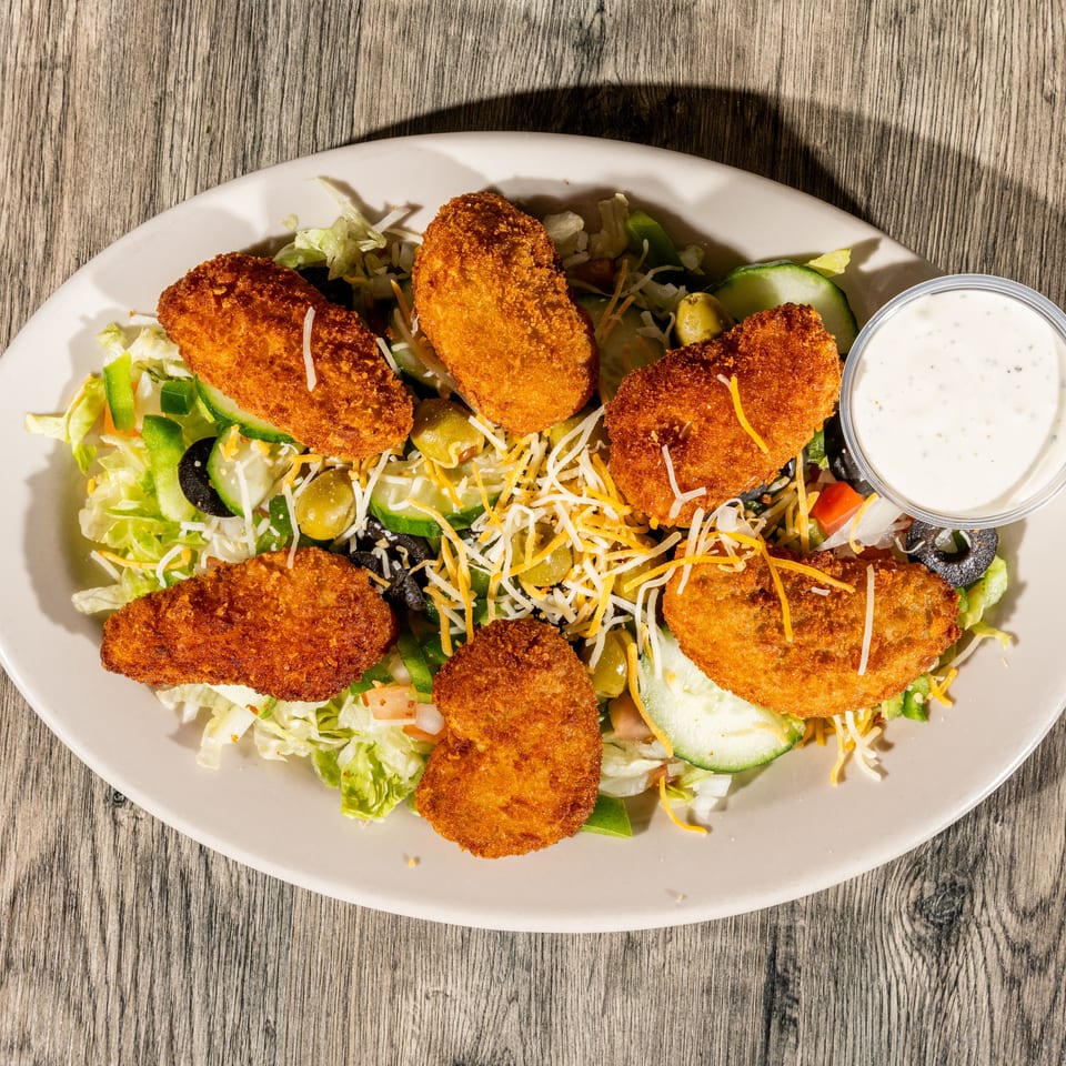 Crispy breaded chicken tenders arranged over a garden salad with shredded cheese, vegetables, olives, and ranch dressing.