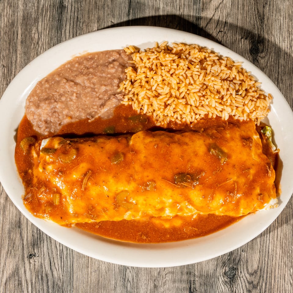 Cheese-covered enchilada smothered in red sauce with refried beans and Mexican rice on a white plate.