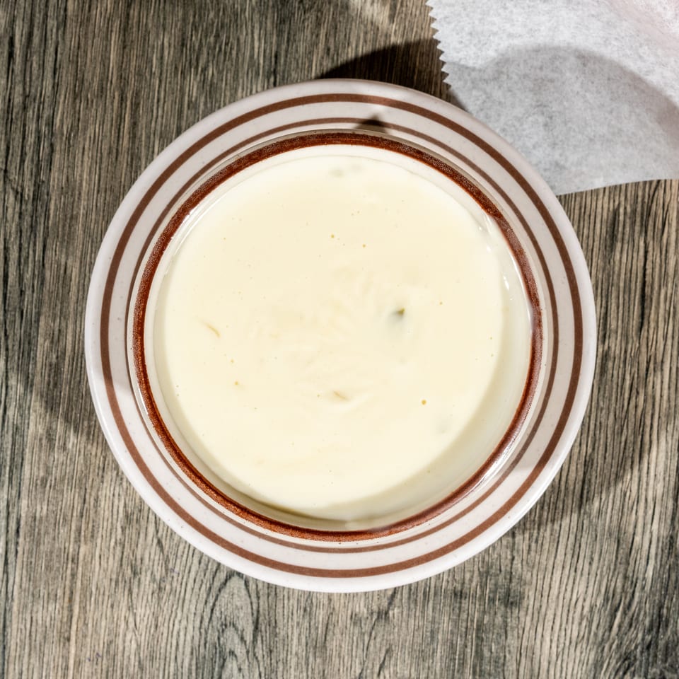 Overhead view of creamy pale soup in a brown-striped bowl on a rustic wooden table beside a napkin.