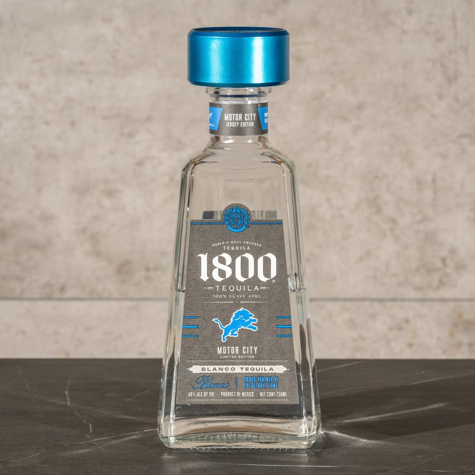 Bottle of 1800 Motor City limited-edition blanco tequila with a bright blue cap on a dark tabletop.