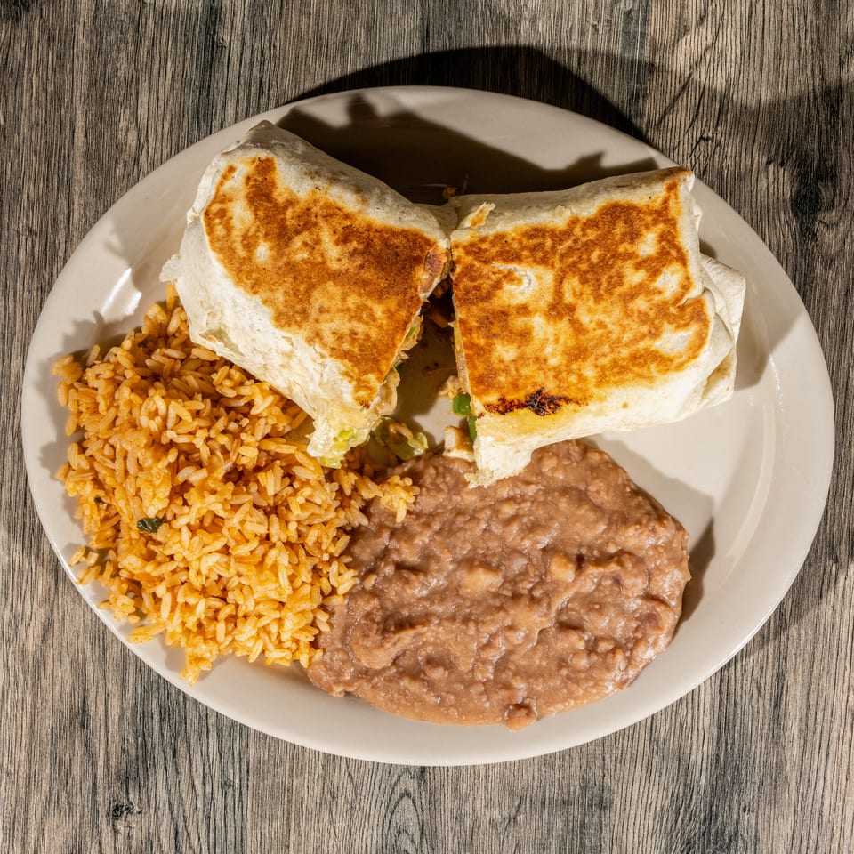 Plate of toasted quesadillas served with Mexican rice and refried beans on a wooden table.