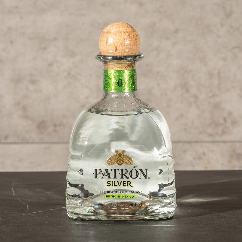 Bottle of Patrón Silver tequila with a wooden stopper displayed on a dark tabletop against a textured wall.