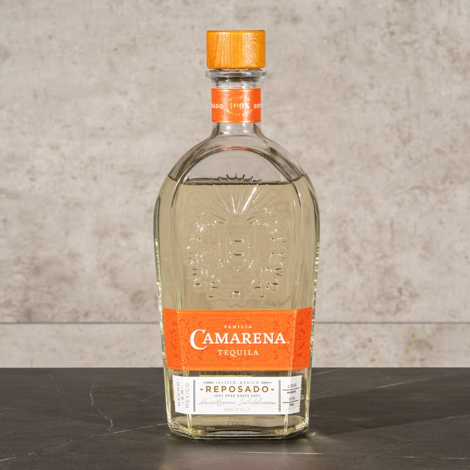 Bottle of Camarena Reposado tequila displayed on a dark table against a textured gray wall.