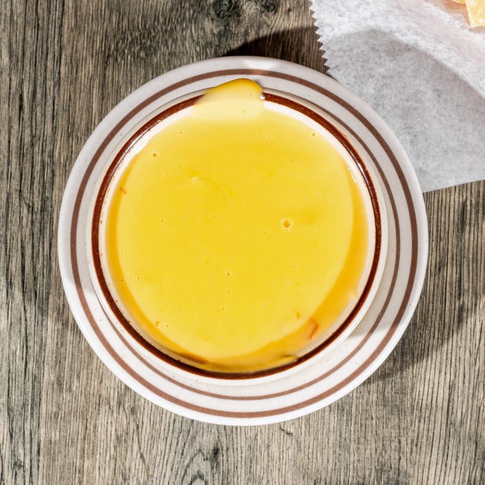 Overhead view of creamy yellow dipping sauce in a striped bowl on a wooden table beside wrapped food.