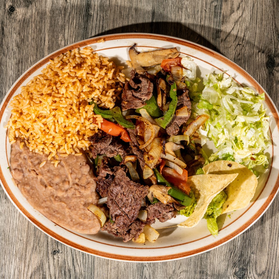 Mexican platter with grilled steak, rice, refried beans, sautéed peppers and onions, lettuce, guacamole, and tortilla chips.